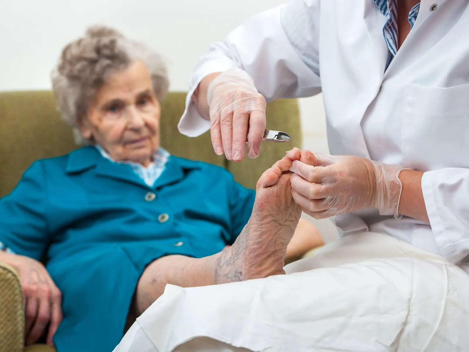 A foot-care practitioner treating an older woman's feet as she sits in her armchair at home